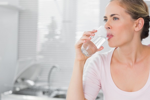 Pensive blond woman drinking water in her kitchen