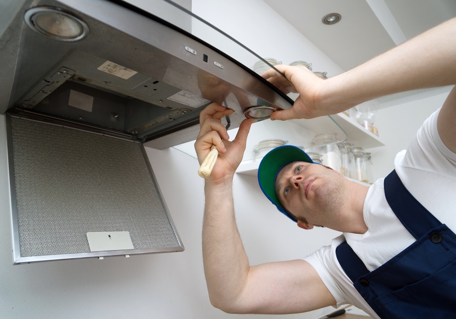 Handsome foreman fixing exhaust hood in the kitchen. Changes the light bulb.