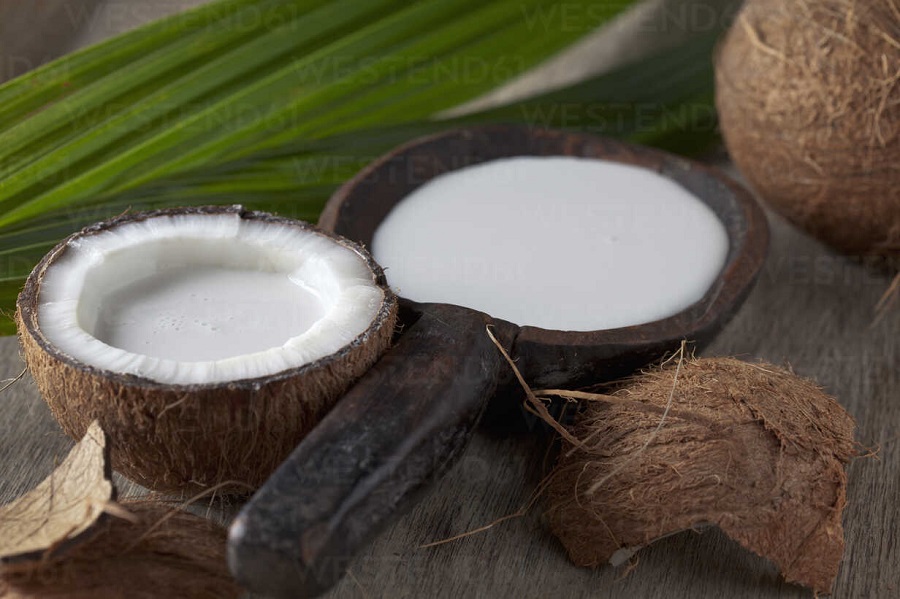 Half coconut with coconut milk in wooden spoon, close up