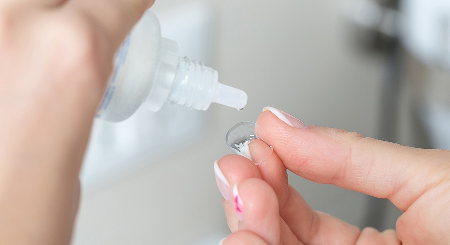 Contact lens on finger and bottle of solution close-up