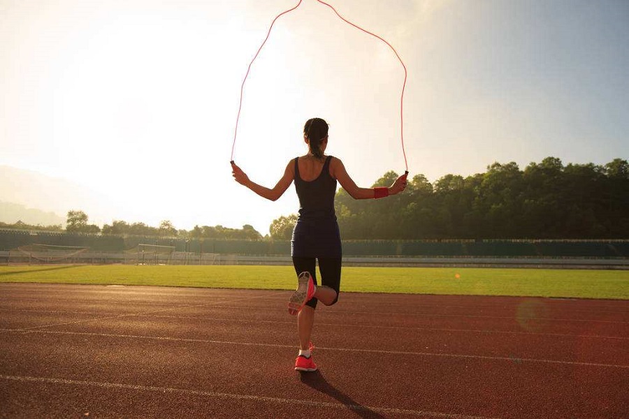 Young woman skipping rope during sunny morning on stadium track