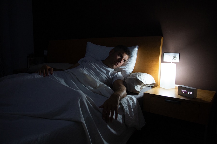 A man with insomnia looks at the clock at dawn from the bed with concern. Lifestyle concept