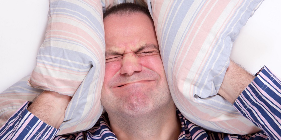 man in pajamas hides her head wih pillow